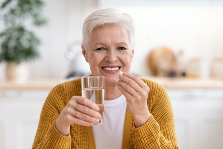 Happy senior lady holding glass of water and pill